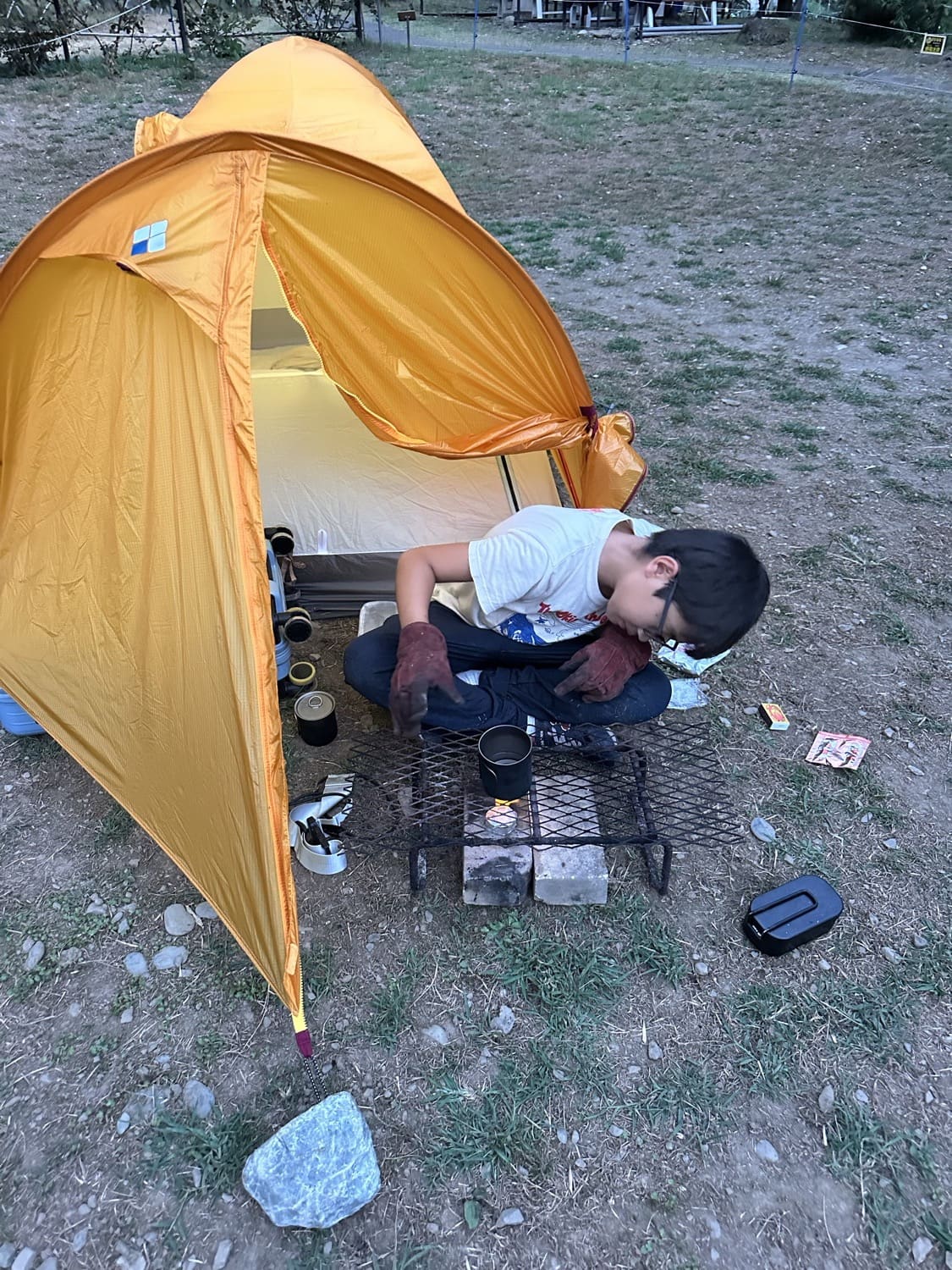 自分のテントの前でバーナーを使って食事をつくる子ども